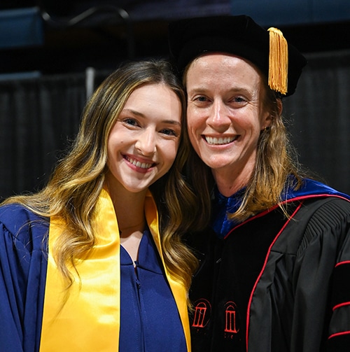 Student and professor smiling in academic regalia at commencement