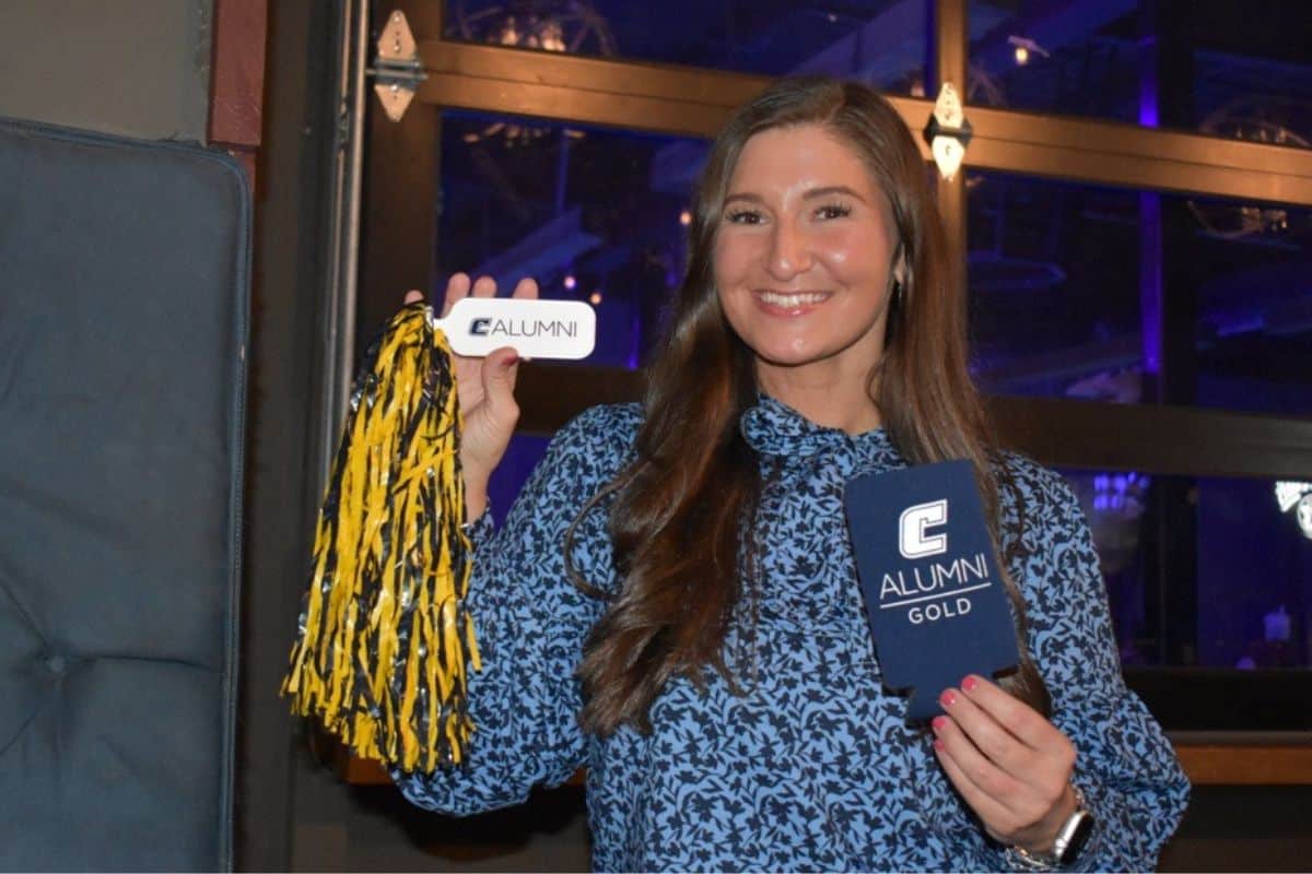 GOLD alumni holding a pom-pom and an alumni-branded koozie.