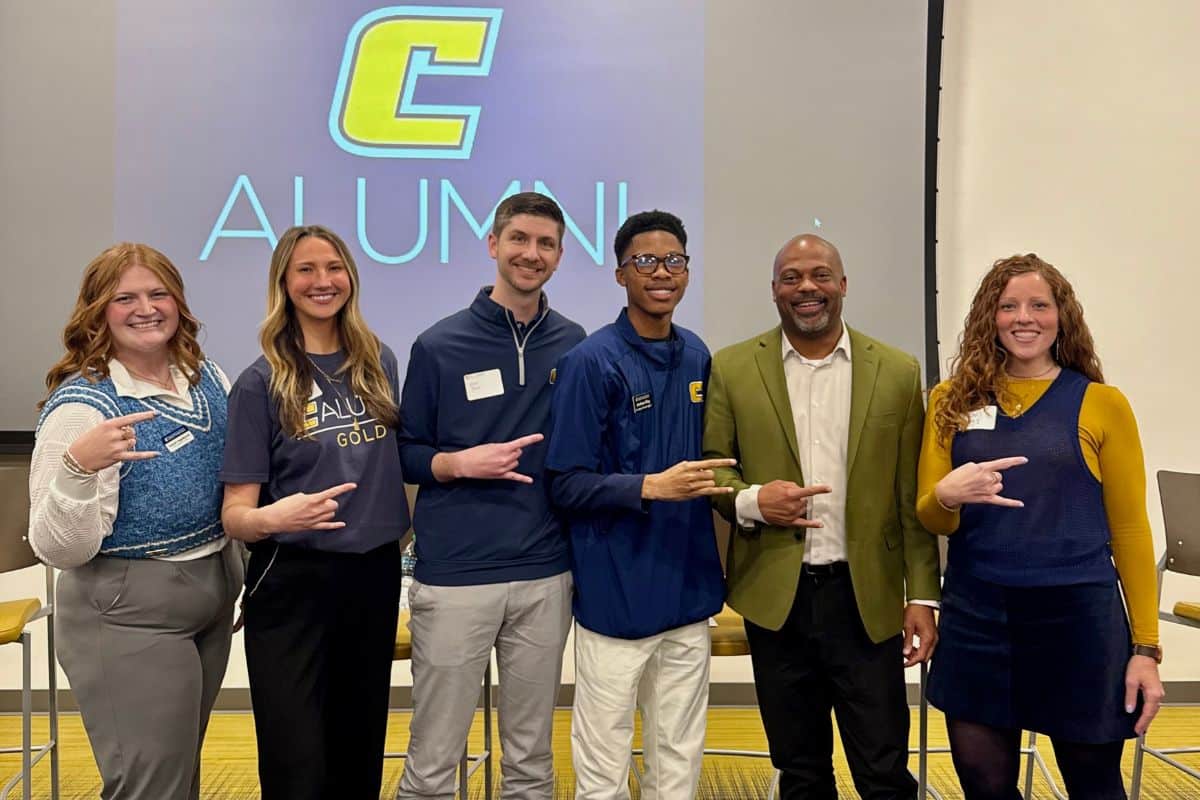 Six alumni standing in front of a PowerPoint screen. 