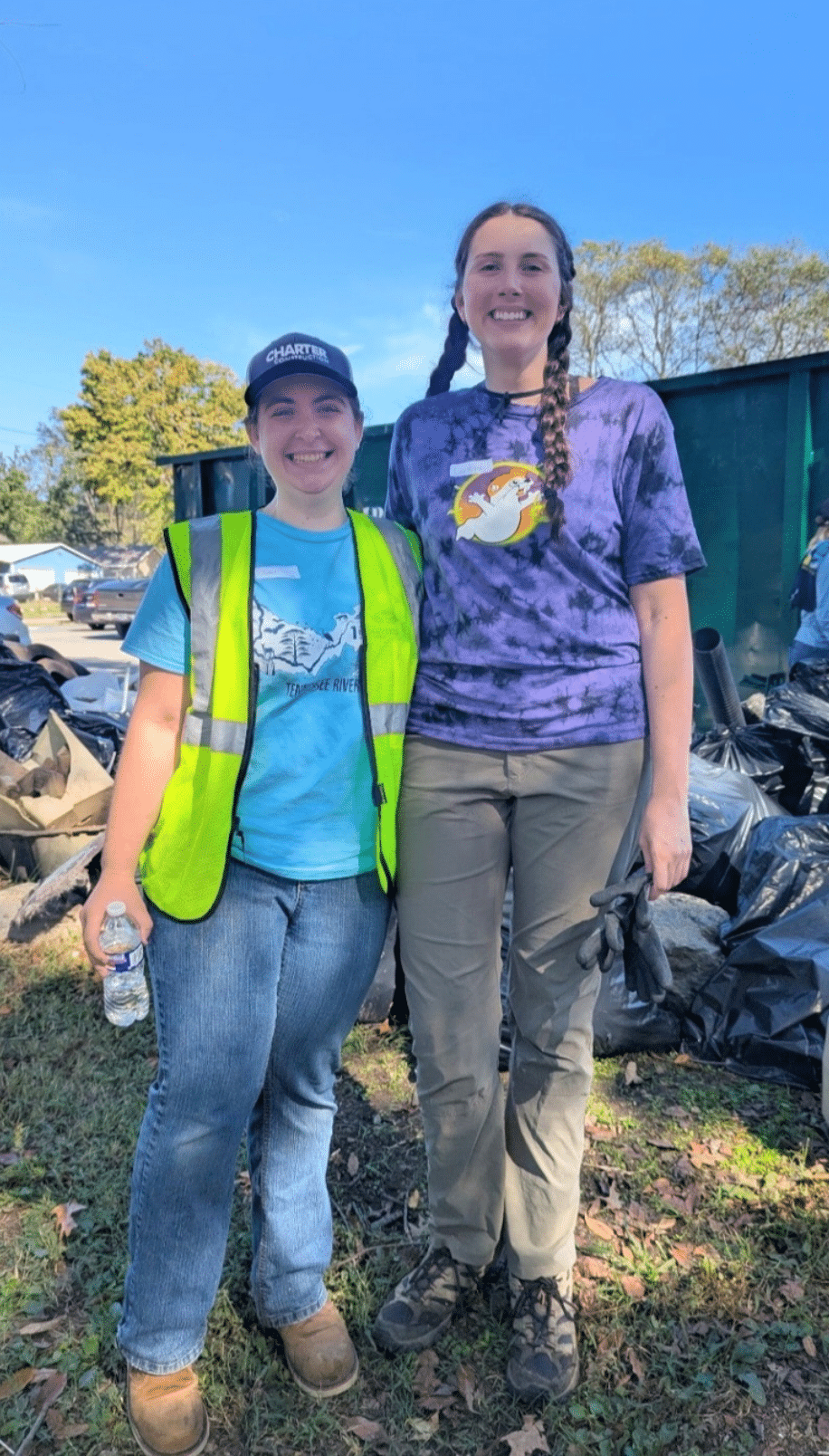 Two people standing together in front of trash bags from a river clean up.