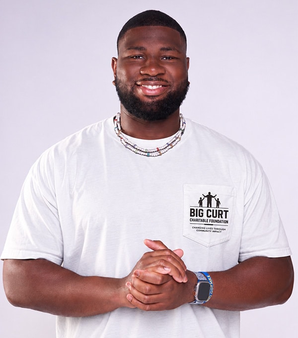 McClendon Curtis in front of a white background, wearing a "Big Curt Charitable Foundation" shirt. 