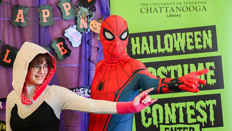 Two students in costumes in front of UTC Library costume contest sign.